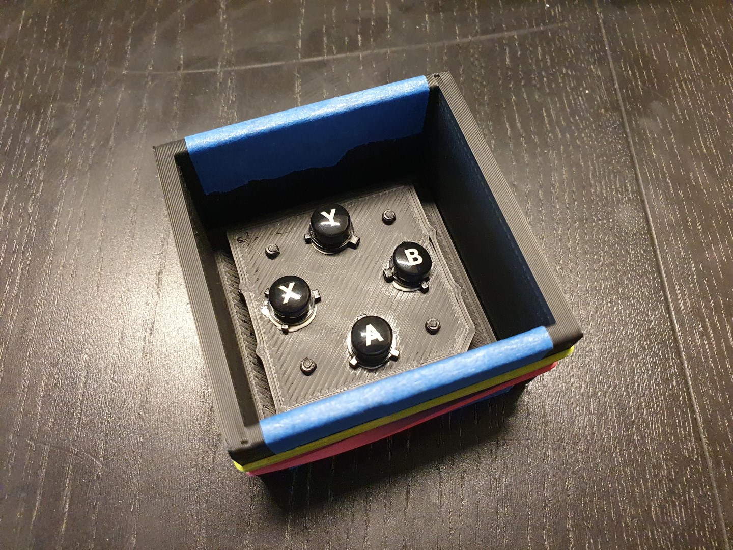 The assembled mold box for the first pour. The buttons are mounted to the bottom. The seems seasled with tape. Two rubber bands go around.