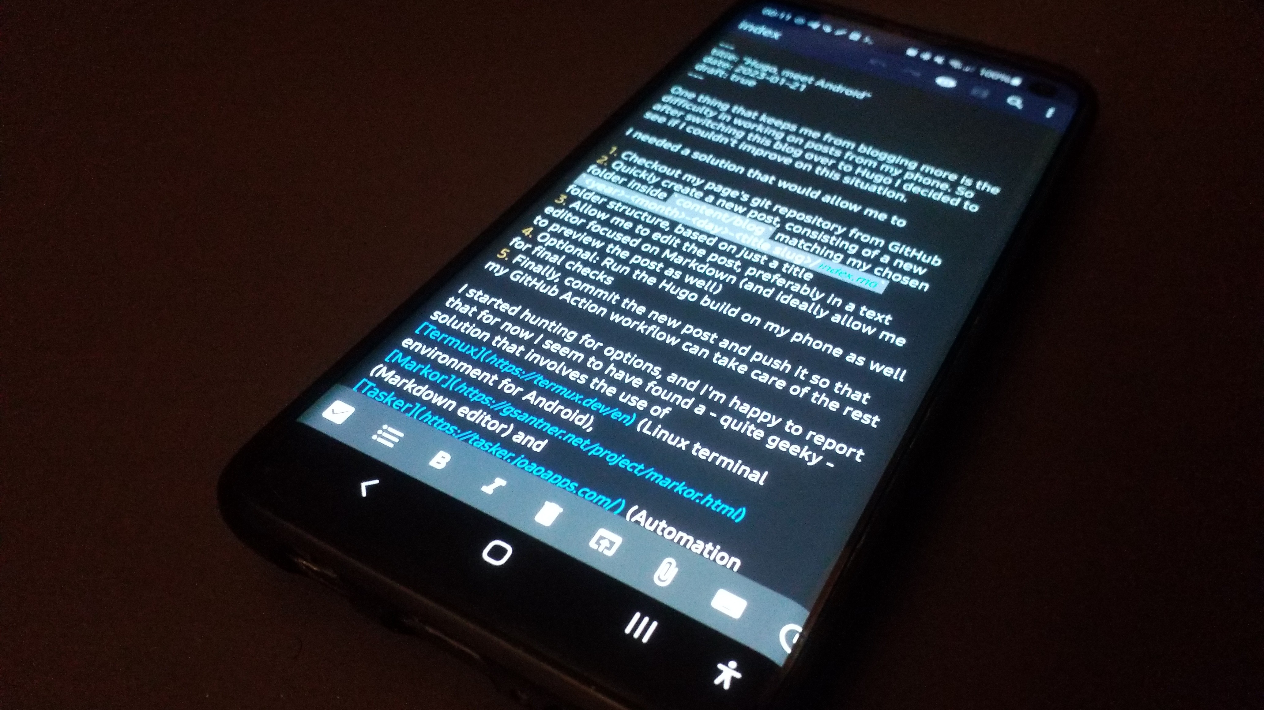 A smartphone lying on a table, showing Markor in editing mode on the Markdown of this blog post.