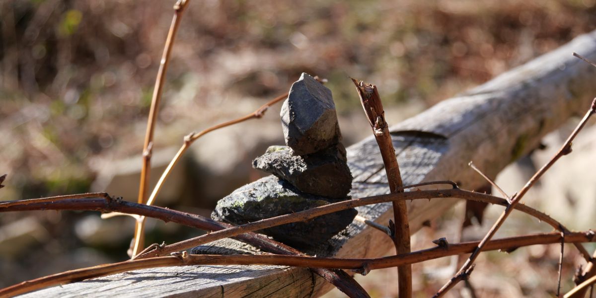 Three stones balancing on each other on a wooden railing somewhere outdoors.